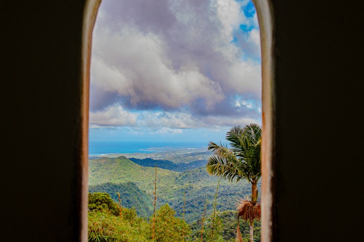 View of lush green valley and cloudy sky through arched window.