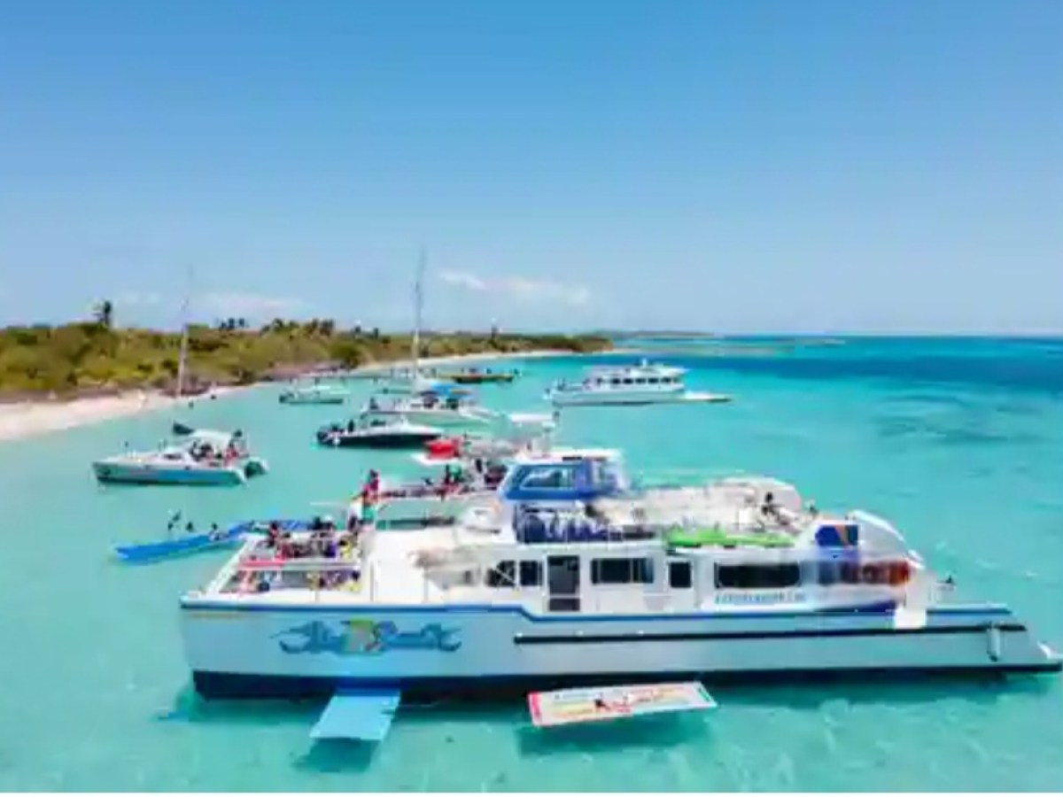 Multiple boats anchored near a tropical beach with clear blue water and green shoreline.